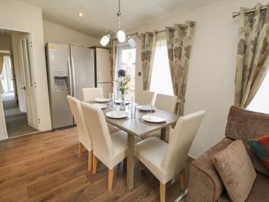 A dining area with a table set for six with white chairs near beige curtains and a stainless steel refrigerator at Bock Retreat in Felton
