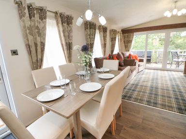 A dining table with six chairs and place settings next to a living room with sofas and large windows at Bock Retreat in Felton
