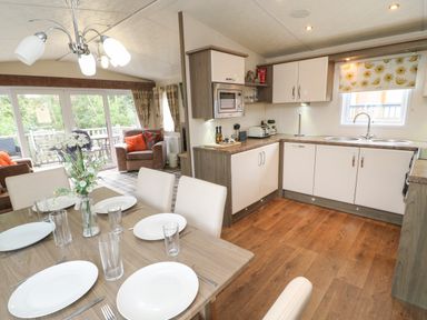 A kitchen and dining area with a wooden table set with plates and glasses next to a seating area with armchairs and large windows at Bock Retreat in Felton