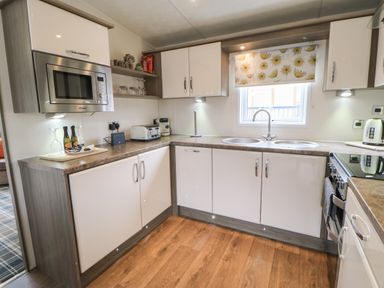 A kitchen with white cabinets wooden floor a microwave toaster coffee machine and a window with floral blind at Bock Retreat in Felton