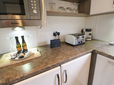 A kitchen countertop with a microwave, toaster, coffee machine, two bottles of prosecco, two wine glasses, and a selection of condiments at Bock Retreat in Felton