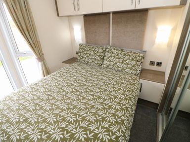 A bedroom with a bed covered in green and white leaf patterned bedding and pillows next to wooden nightstands with wall lights and a window with curtains at Bock Retreat in Felton