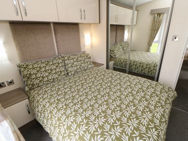 A bedroom with a bed with leaf-patterned bedding two bedside tables and mirrored wardrobe at Bock Retreat in Felton