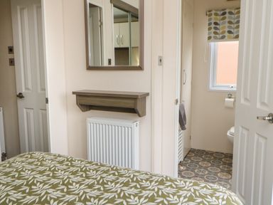 A bedroom with a patterned bedspread a mirror and shelf above a radiator and a view into a bathroom at Bock Retreat in Felton