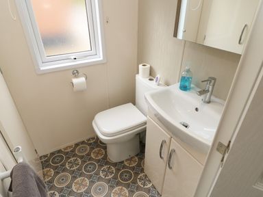 A small bathroom with a toilet next to a sink with cabinet and frosted window at Bock Retreat in Felton