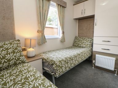 A bedroom with two single beds with green leaf patterned bedding a bedside table with a lamp a window with curtains and built in wardrobes at Bock Retreat in Felton