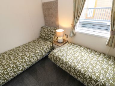 A bedroom with two single beds with leaf patterned bedding a nightstand with a lamp and a window with curtains at Bock Retreat Felton