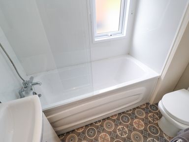 A bathroom with a bathtub shower combination a sink and a toilet with patterned floor tiles at Bock Retreat in Felton