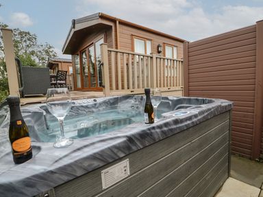 An outdoor hot tub with two bottles of prosecco and two wine glasses near a wooden cabin at Bock Retreat in Felton