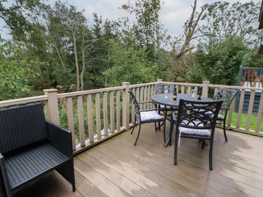 An outdoor deck with a black wicker chair and a round table with four chairs and glasses near trees at Bock Retreat in Felton