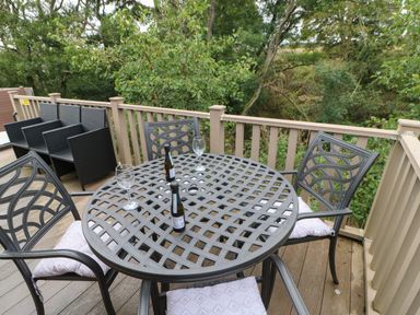 An outdoor wooden deck with a round metal table and four chairs with cushions and two bottles and two glasses on the table at Bock Retreat in Felton