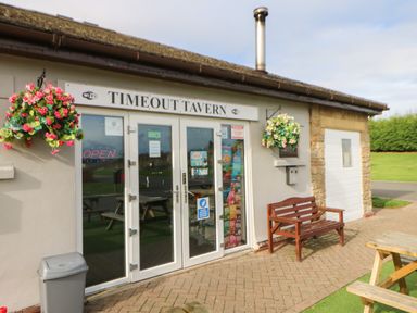 Exterior of Timeout Tavern with glass doors a wooden bench hanging flower baskets and outdoor picnic tables at Bock Retreat in Felton