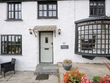 The exterior of a white stone cottage with black framed windows a grey door and a potted plant at Church View Cottage Near Looe