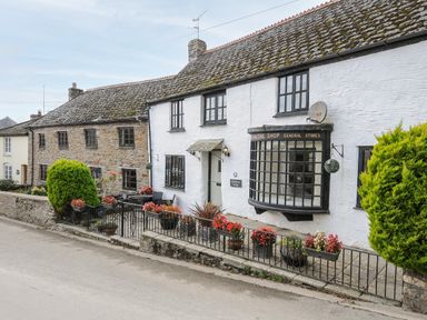 A street view of stone and white cottages with flower pots along a metal fence at Church View Cottage Near Looe