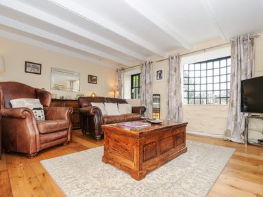 A living room with leather armchairs sofa wooden coffee table large window and television at Church View Cottage Near Looe