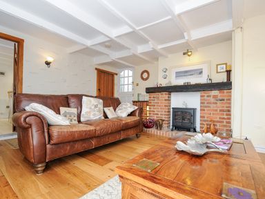 A living room with a brown leather sofa pillows a wooden coffee table and a brick fireplace at Church View Cottage Near Looe