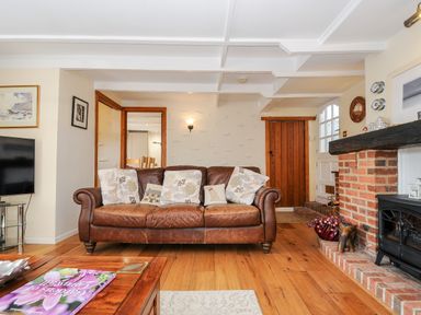 A living room with a leather sofa pillows wooden floor and a brick fireplace at Church View Cottage Near Looe
