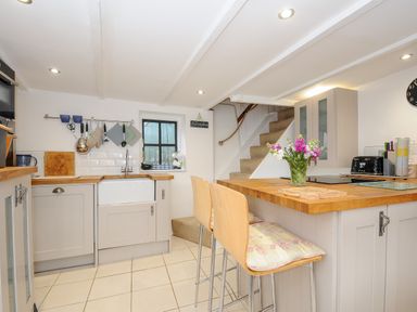 A kitchen with wooden countertops stools flowers on the island and stairs at Church View Cottage Near Looe