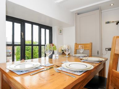 A dining table set with plates glasses and cutlery near a window with black frames at Church View Cottage Near Looe