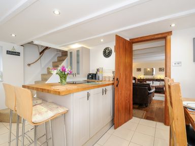 A kitchen area with bar stools and a wooden countertop next to a doorway leading to a living room at Church View Cottage Near Looe