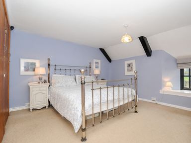 A bedroom with a metal frame bed two bedside tables with lamps light blue walls and a window at Church View Cottage Near Looe