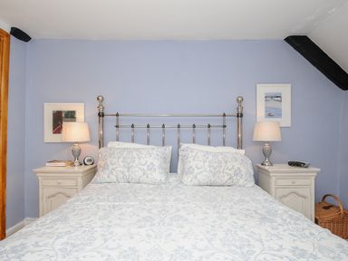 A bedroom with a metal bed frame blue patterned bedding two bedside tables with lamps and framed pictures on a blue wall at Church View Cottage Near Looe