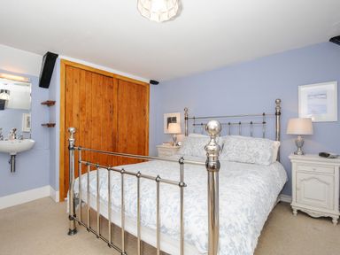 A bedroom with a metal bed frame blue floral bedding wooden wardrobe sink and two bedside tables with lamps at Church View Cottage Near Looe