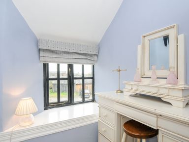 A room with a dressing table mirror perfume bottles lamp and window with patterned blinds at Church View Cottage Near Looe