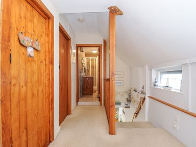 A carpeted hallway with wooden doors and a bathroom at the end with a staircase and small window on the right at Church View Cottage Near Looe