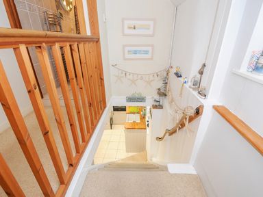 A stairway with wooden banister and nautical decorations leading down to a kitchen at Church View Cottage near Looe