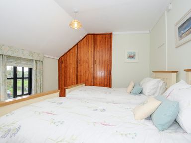 A bedroom with two single beds with floral bedding and a wooden wardrobe at Church View Cottage Near Looe