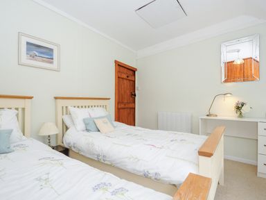 A bedroom with two single beds a wooden door a desk with a lamp and a mirror at Church View Cottage Near Looe