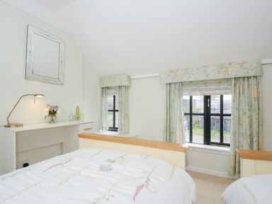A bedroom with two beds floral curtains a desk with lamp and flowers at Church View Cottage Near Looe