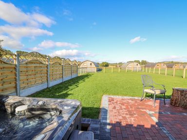 A backyard with a hot tub patio chair grassy field wooden fence and small wooden cabins at Poppy in St Harmon near Rhayader