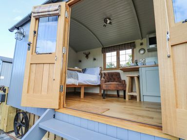An open door showing a small room with a bed, armchair, window, and kitchenette at Poppy in St Harmon near Rhayader