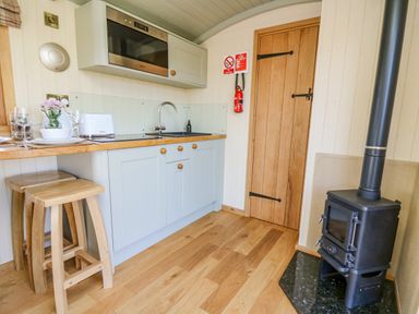 A compact kitchen area with wooden stools a microwave sink wooden cabinets and a black stove at Poppy in St Harmon near Rhayader