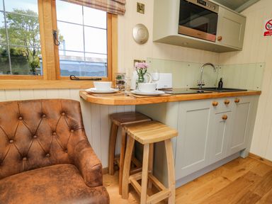 A small kitchen area with a wooden countertop set for two and leather chair at Poppy St Harmon near Rhayader