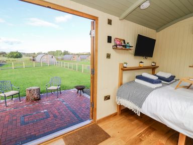 A bedroom with a bed folded towels a wall-mounted TV and an open door leading to a patio with chairs and green grass at Poppy St Harmon near Rhayader