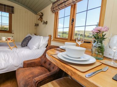 A small bedroom with a bed cups on a tray a wooden table with plates bowls and a flower vase at Poppy St Harmon near Rhayader