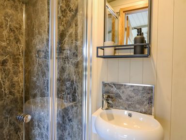 A bathroom with a round sink faucet mirror and a shower with stone-patterned walls at Poppy in St Harmon near Rhayader