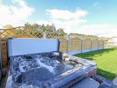 An outdoor hot tub with water bubbling next to a wooden fence and green grass at Poppy in St Harmon near Rhayader