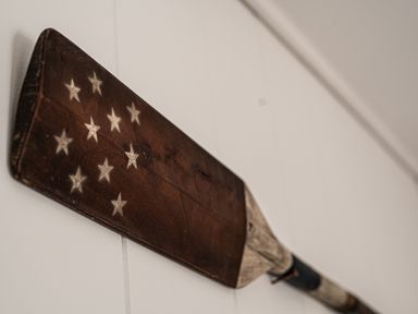 A close up of a weathered wooden paddle with white stars painted on it mounted on a white wall at Galwad y Mor in Niwbwrch newborough