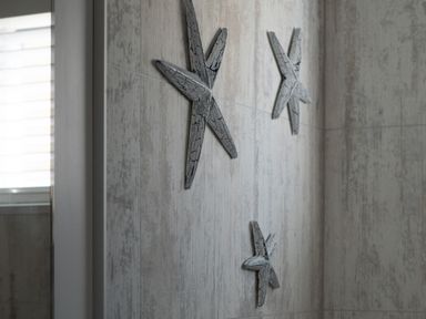 Three decorative starfish mounted on a tiled wall near a window at Galwad y Mor in Niwbwrch newborough