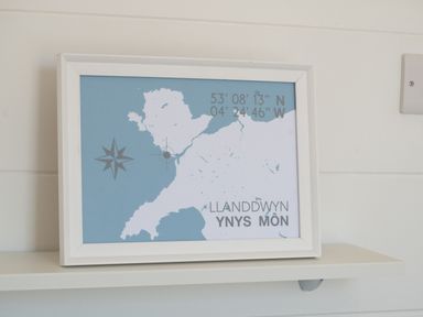 A framed map of Llanddwyn Ynys Mon with coordinates on a white shelf