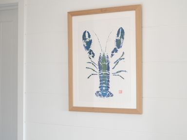 A framed artwork of a blue lobster on a white wall at Galwad y Mor in Niwbwrch newborough