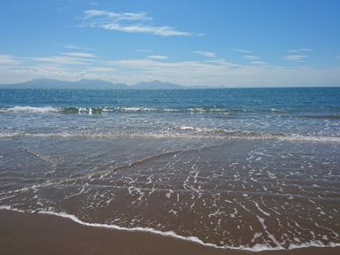 A sandy beach with waves and the sea under a blue sky at Galwad y Mor in Niwbwrch newborough
