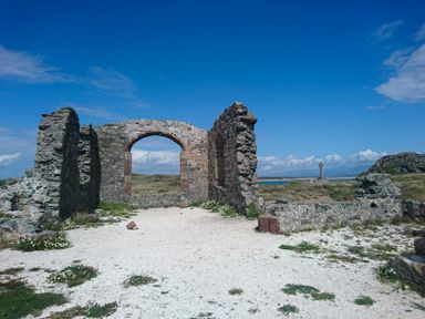 Ruins of a stone building with an arched window and grassland under a blue sky at Galwad y Mor in Niwbwrch newborough