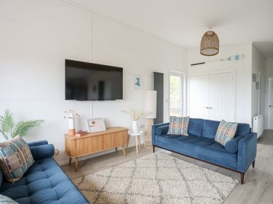 A living room with two blue sofas a wall mounted television and a wooden cabinet at Galwad y Mor in Niwbwrch newborough