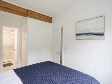A bedroom with a bed covered by a blue blanket two open doors and a painting on the wall at Galwad y Mor in Niwbwrch newborough