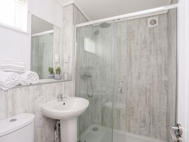 A bathroom with a shower enclosure sink toilet towels and small plants at Galwad y Mor in Niwbwrch newborough